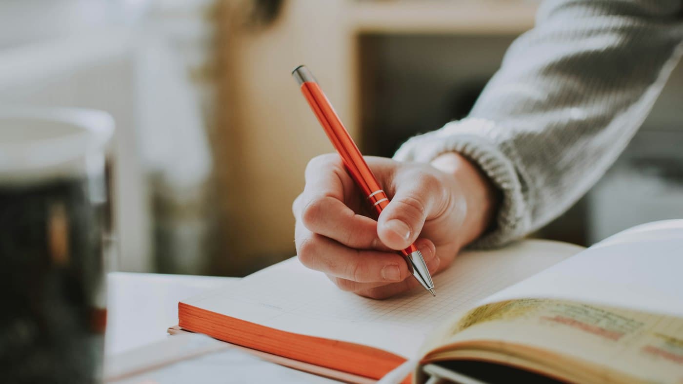 Teacher marking written English work with a red pen against rubric criteria